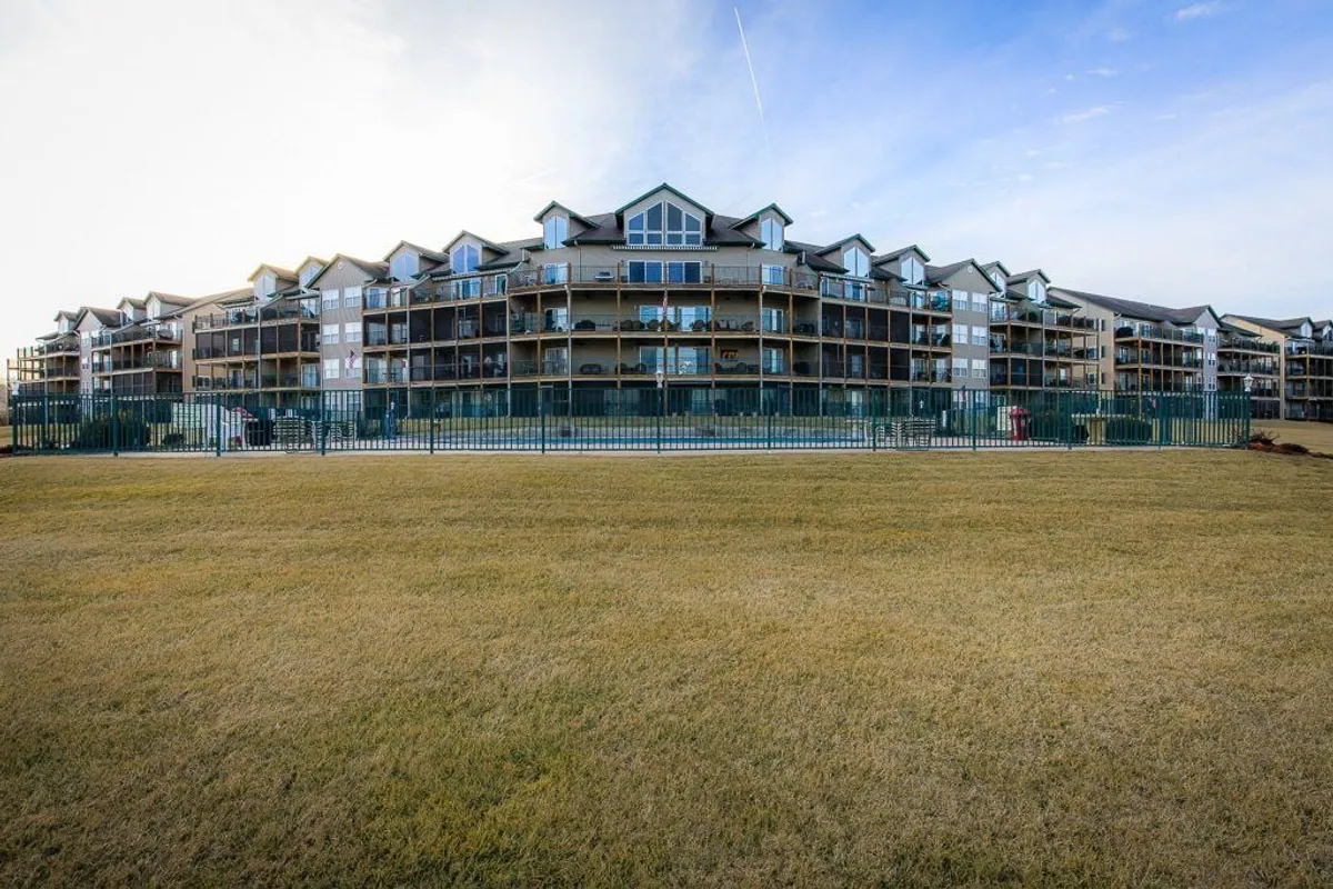 A multi-story building with balconies overlooking a green, fenced lawn. The communal outdoor space is perfect for picnics, casual games, or simply soaking in the lake atmosphere. The scene suggests a welcoming environment for both kids and adults to gather and play.