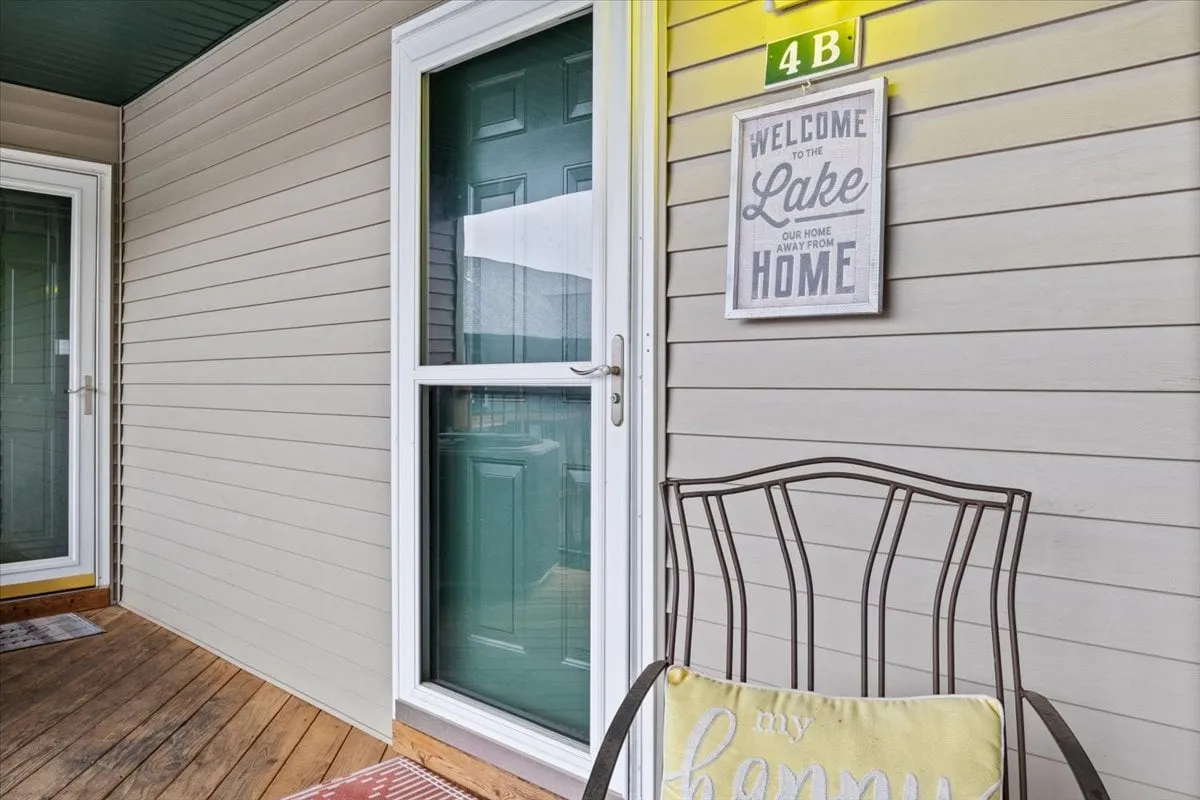 This exterior image features a porch with a green door, a welcome sign, and a comfortable chair with a cushion. The scene suggests peaceful mornings and evenings spent enjoying the outdoors, perfectly aligning with the lakeside and fishing retreat vibe.