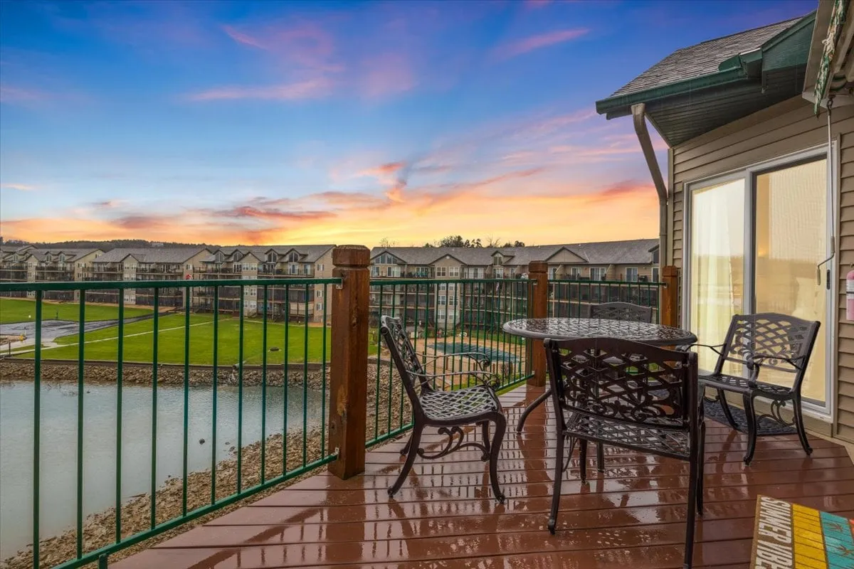 A serene exterior shot featuring an outdoor dining set on a private patio overlooking the lake, with a vivid sunset sky in the background. The table is set for a meal, offering a perfect spot for alfresco dining and sunset watching.