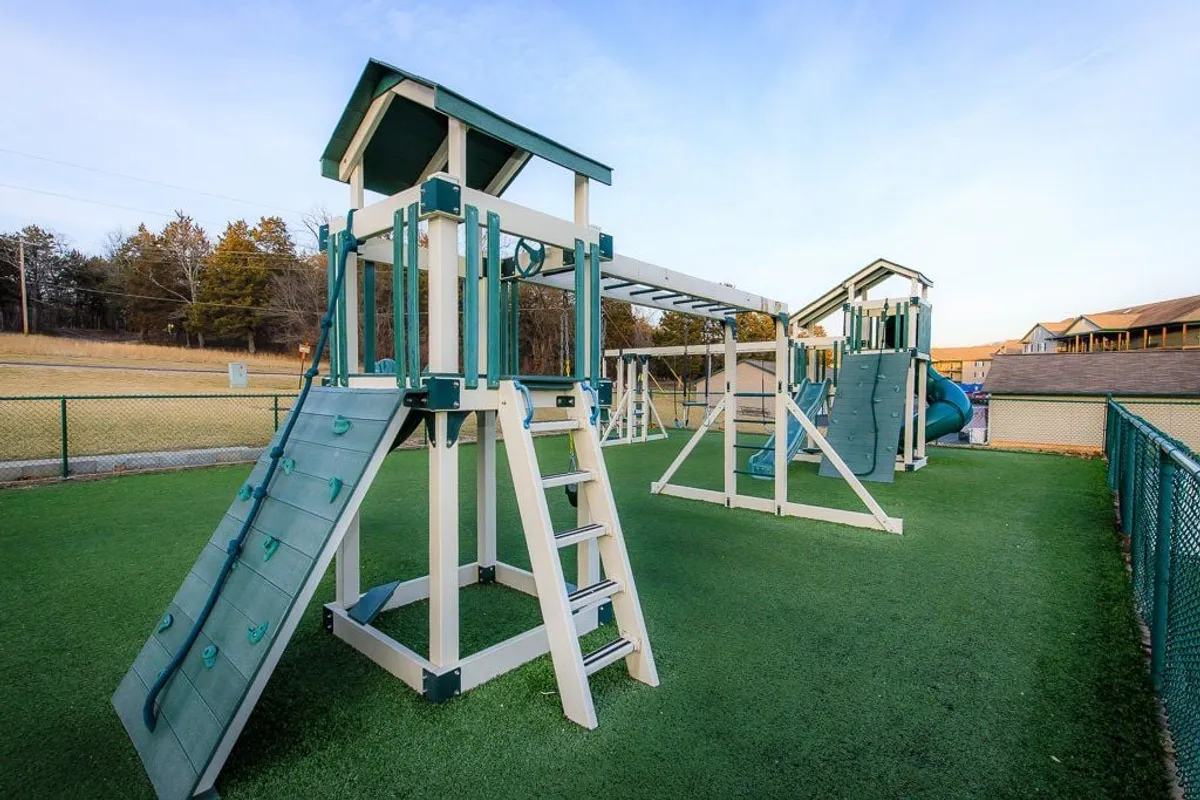 A vibrant playground structure with a slide and climbing area set on a green lawn, designed for children’s play and family gatherings. The scene is lively and joyful, capturing the sense of community and safe play for kids.