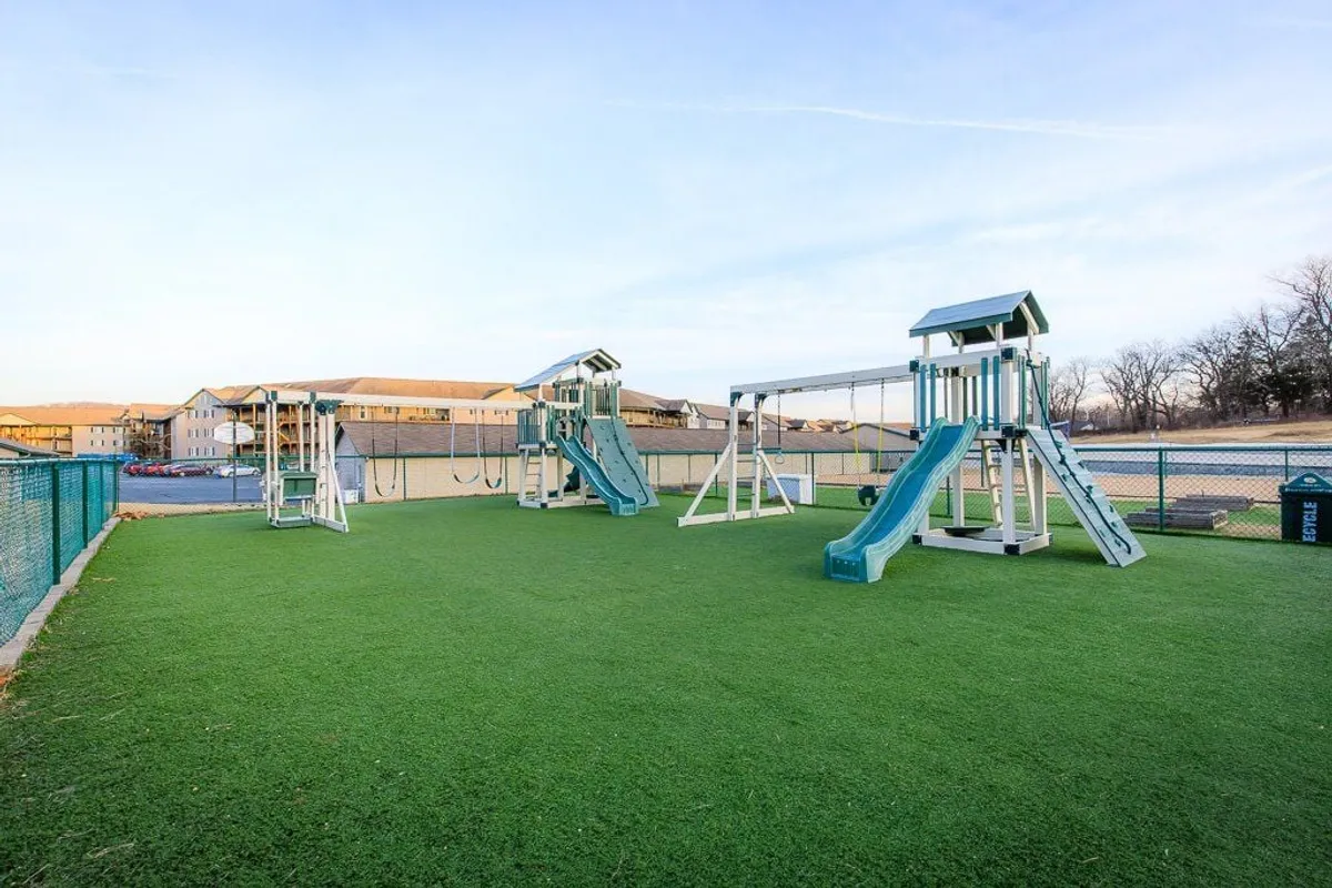 A cheerful playground featuring a swing set and colorful equipment, set on lush green grass. The inviting environment is designed for kids to play and families to connect in a secure outdoor space.