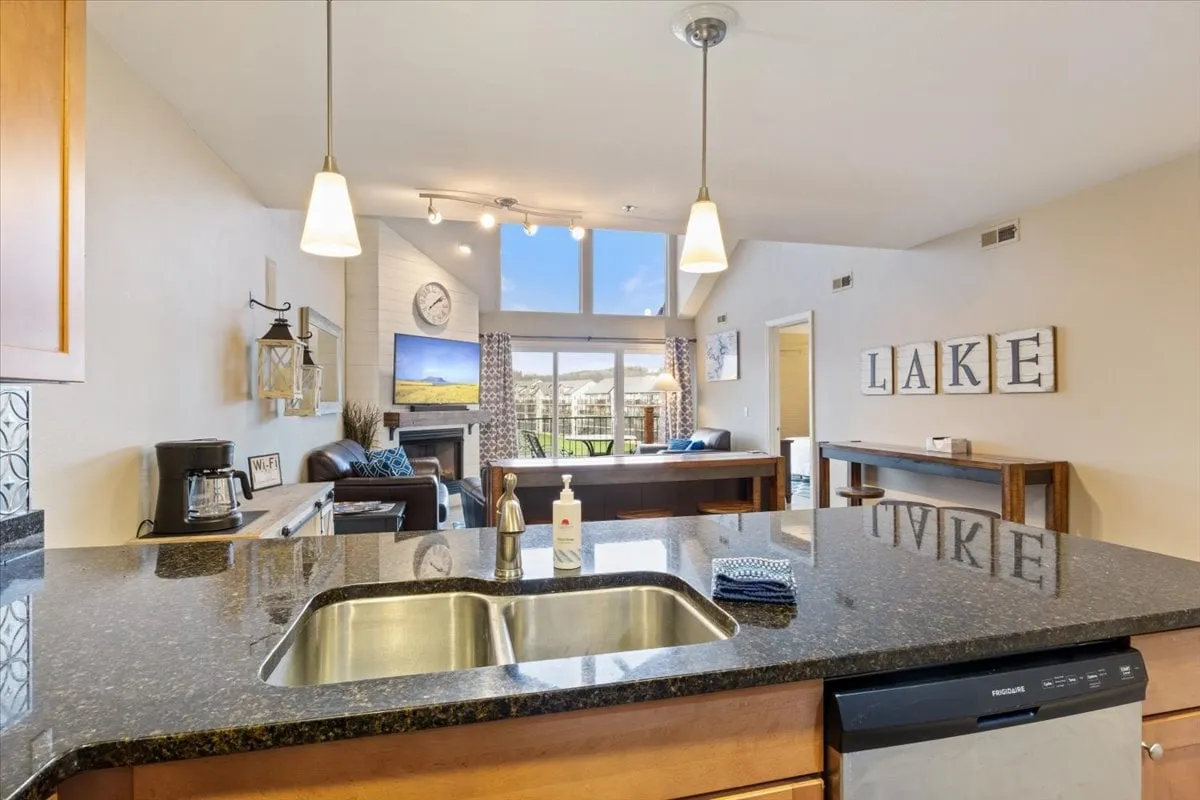 An open-concept space showcasing a kitchen island, living area, and large windows overlooking the lake. Decorative wall letters add a touch of personality, while the layout connects the kitchen and living room, making it ideal for entertaining or family meals. The lake view is visible from multiple vantage points, blending indoor comfort with scenic beauty.