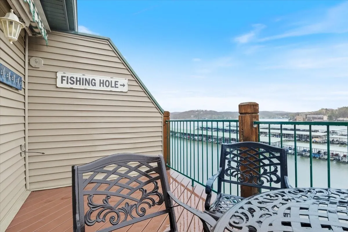A cozy patio corner with outdoor seating, a 'Fishing Hole' sign, and an expansive lake view in the background. The atmosphere is tranquil and inviting, ideal for unwinding, socializing, or enjoying the beauty of the lakeside setting.
