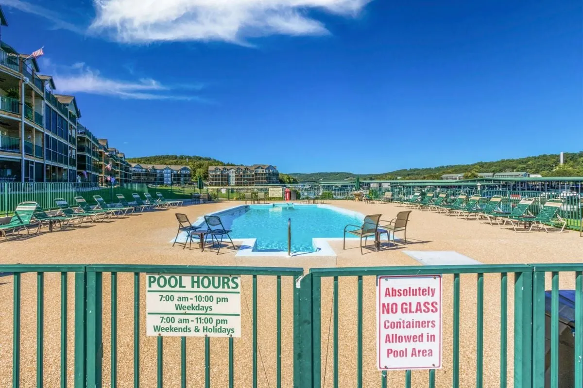 A sparkling outdoor swimming pool surrounded by lounge chairs and a welcoming sign, set in a relaxed resort atmosphere. The area invites guests to enjoy sunny swims, relax by the water, and socialize in a vibrant communal space.