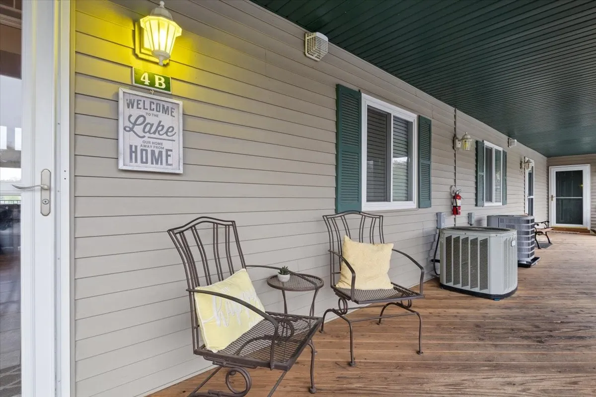 This image shows a welcoming patio area with a 'welcome' sign, lawn chairs with decorative pillows, and a light fixture. The setting evokes a tranquil and inviting atmosphere, suggesting an ideal spot to relax with a view of the lake after a day on the water.